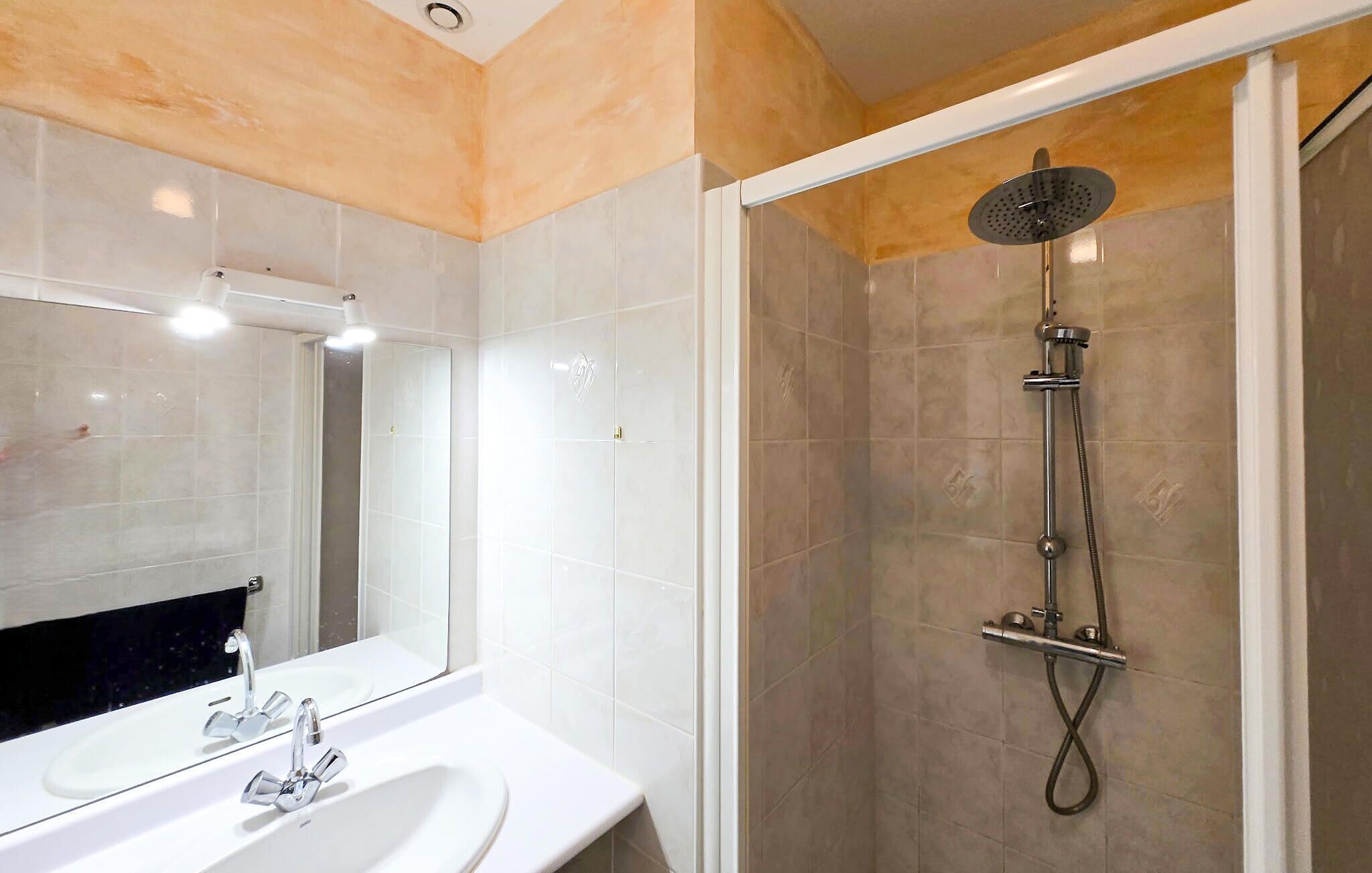 Ein modernes Badezimmer mit einem weißen Waschbecken, einem großen Spiegel und einer Duschkabine.