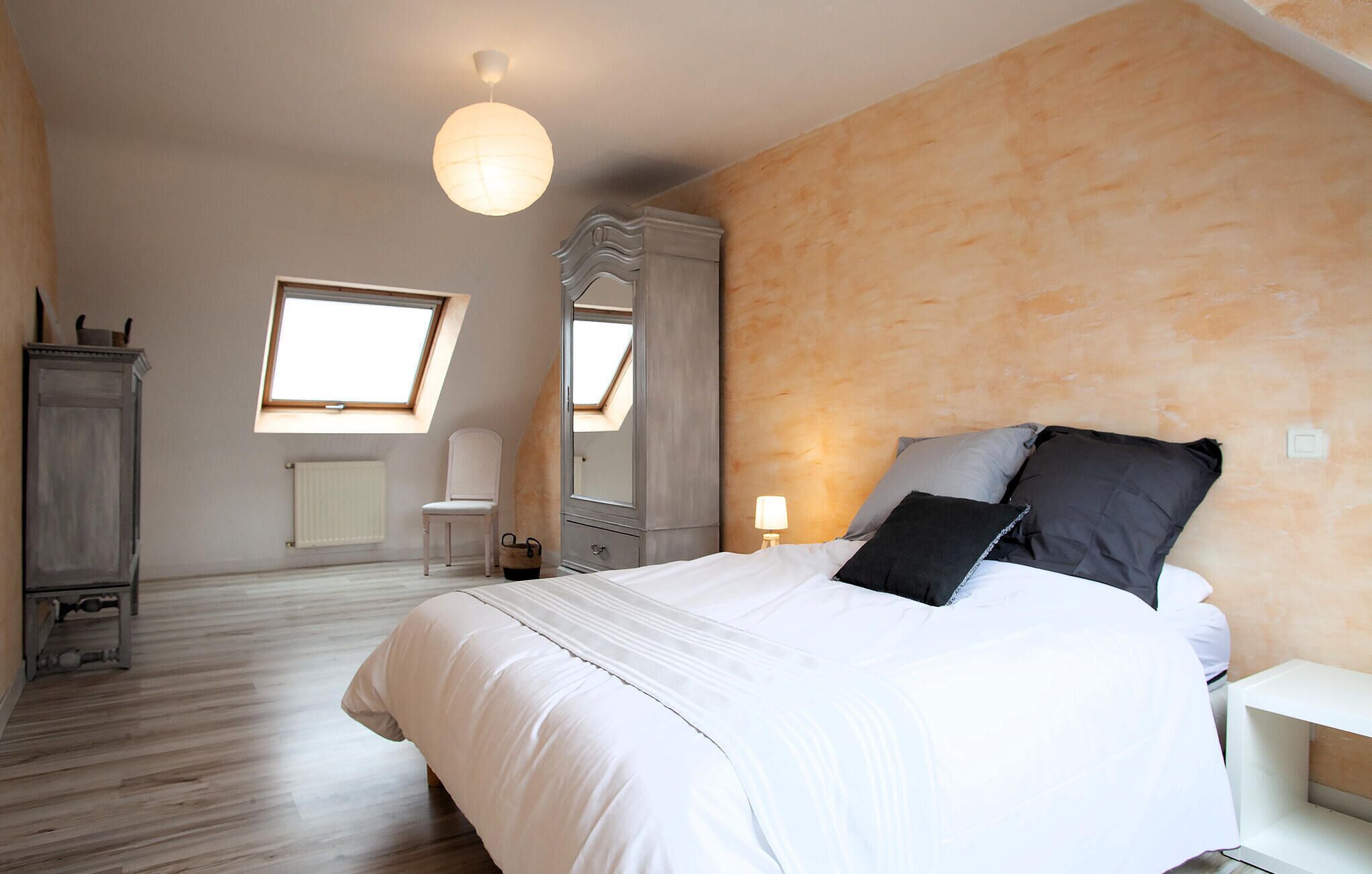 A bedroom with a large bed, a dresser, a chair, a window, and a mirror.