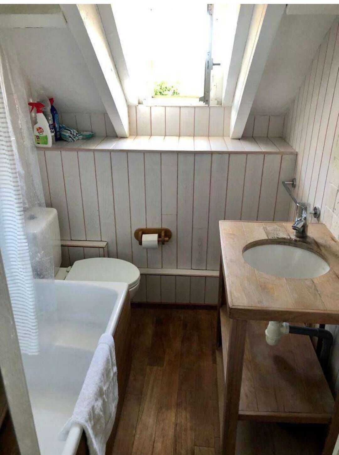Een kleine, smalle badkamer met een houten wastafel, een wit toilet en een bad.