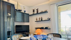 Un coin repas avec une table dressée pour deux personnes, un téléviseur et des objets décoratifs disposés sur des étagères.