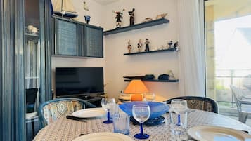 Een eethoek met een tafel gedekt voor twee personen, een televisie en decoratieve objecten op planken.