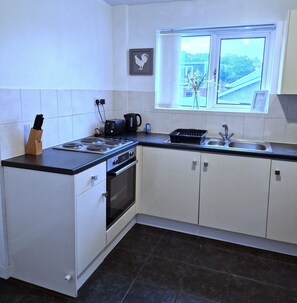 A kitchen with white cabinets, a black countertop, a stove, a sink, and a window with a view of greenery.