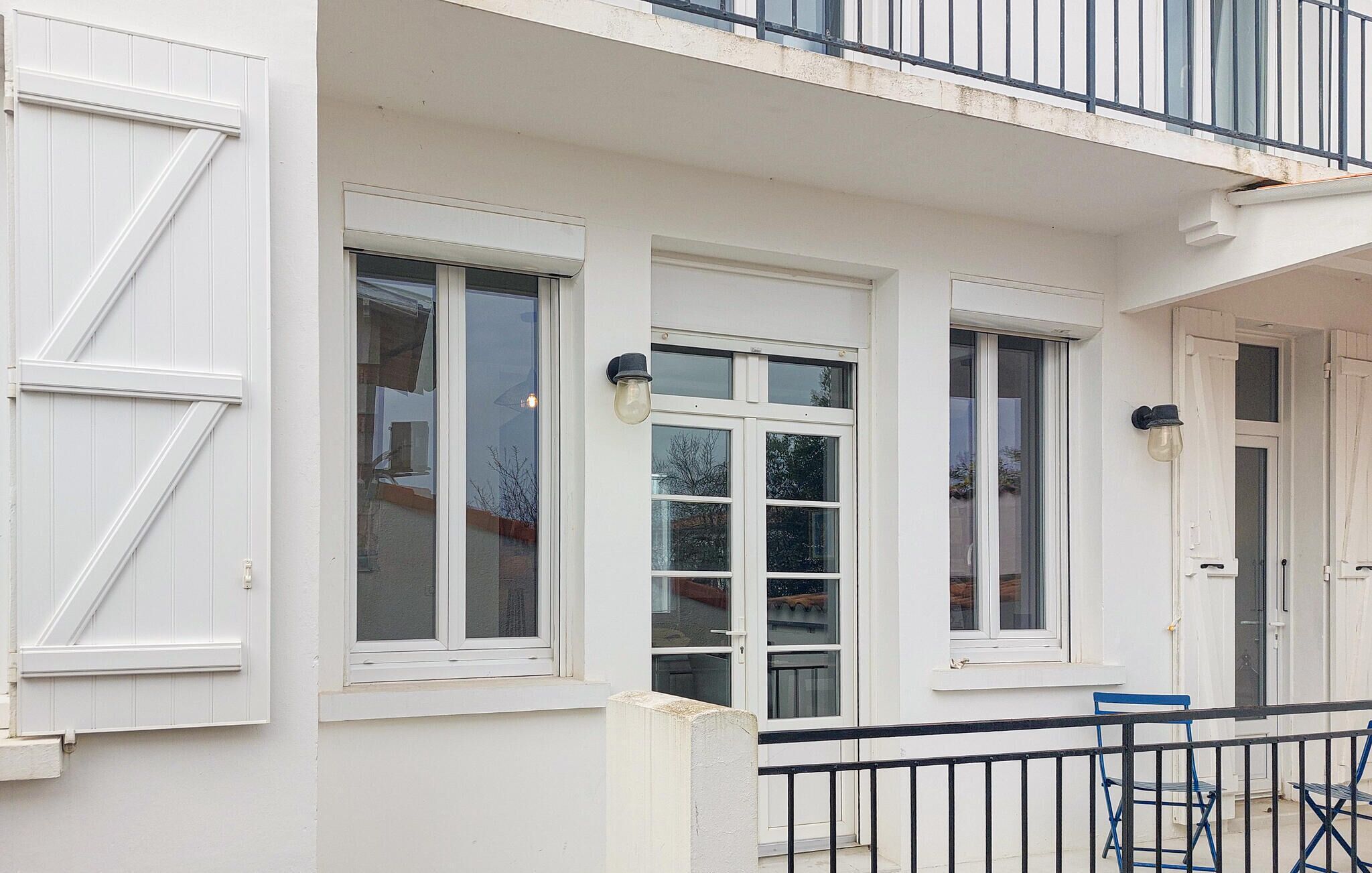Ein weißes Gebäude mit großen Fenstern, einem Balkon mit schwarzer Geländer und einer Tür mit einer schwarzen Leuchte im Hutstil.