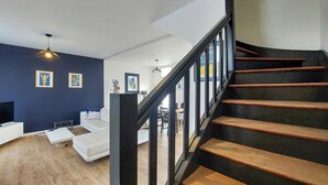 A modern living room with a staircase, wooden flooring, and a dark blue accent wall. - Charmante maison proche mer (Royan)