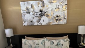 Une chambre d’hôtel avec un lit agrémenté d’une couvre-lit sur le thème de la mer, une grande peinture abstraite au mur et deux lampes de chevet.