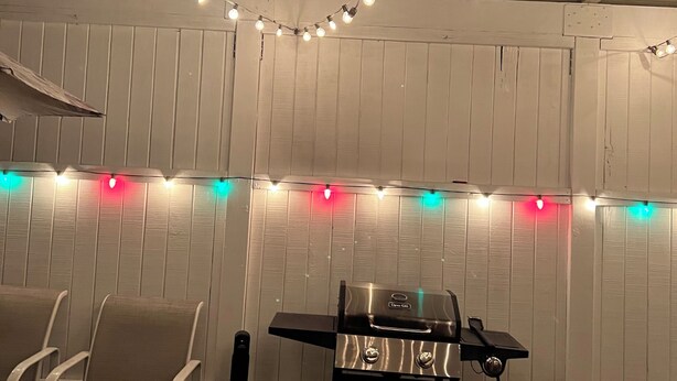 Un jardin avec un barbecue, des guirlandes lumineuses et un canapé rouge.