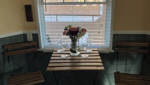 Un coin repas avec une table dressée pour quatre personnes, un vase de fleurs et une fenêtre avec des stores.