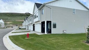 Une rangée de maisons de ville à un étage, avec des garages attenants, un potelet d’incendie rouge et une pancarte « À louer ».