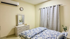 Een slaapkamer met een bed, een kaptafel, een spiegel, een airconditioner en een klok aan de muur.