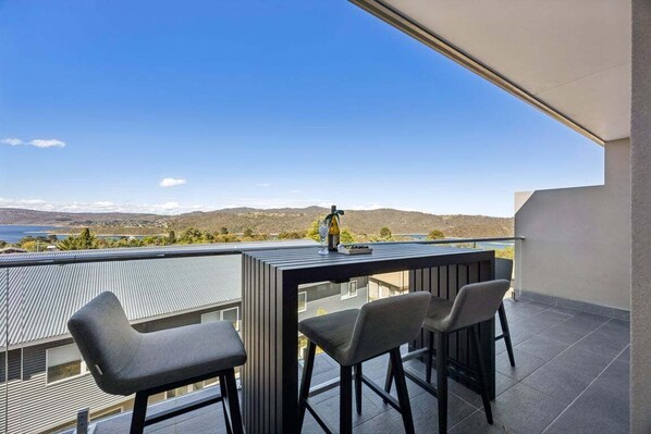 A balcony with a table and two chairs, overlooking a scenic landscape with mountains and a body of water.