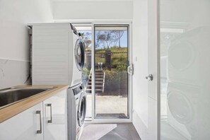 A compact kitchen with a built-in washer and dryer, a wooden countertop, and a sliding glass door leading to a backyard.