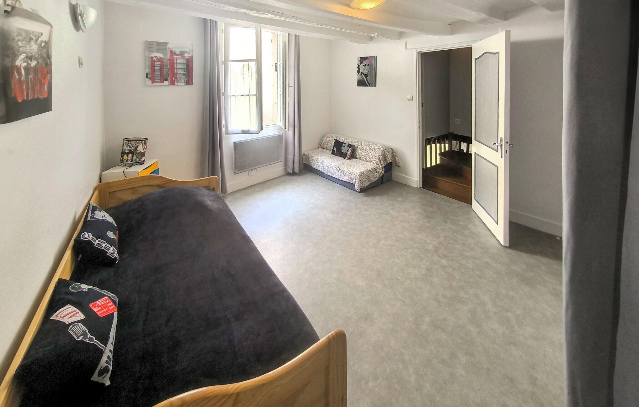 A bedroom with a bed, a sofa, a window, and a door leading to another room.