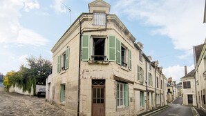 Un edificio storico con persiane verdi, una strada acciottolata e un'auto parcheggiata.