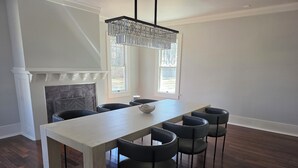 Un'area pranzo con un lungo tavolo, sei sedie, un lampadario moderno, un camino e ampie finestre.