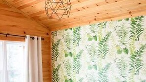 A room with wooden walls, a patterned wallpaper, a wooden dining table with chairs, and a dark-colored sofa. - The Pine, Lawrencetown (West Porters Lake)