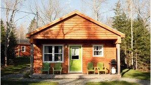 A small wooden cabin with a green door, two windows, and two green Adirondack chairs outside. - The Pine, Lawrencetown (West Porters Lake)