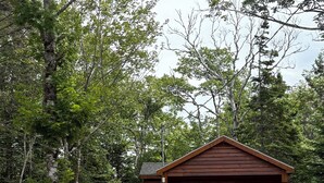 A cabin with a gravel driveway, surrounded by trees and large rocks. - The Redwood Studio - Lawrencetown Lodge (West Porters Lake)