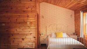 Habitació d'una cabana de fusta amb un llit, una tauleta de nit i una taula petita.