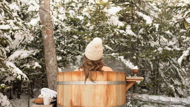 Una persona relaxant-se en una sauna de fusta envoltada d'arbres coberts de neu.