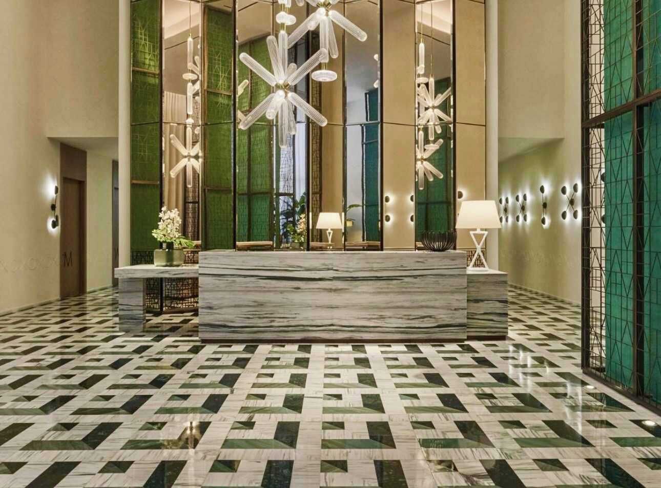 Un hall d’entrée doté d’un comptoir de réception en marbre, d’un sol à motifs et de luminaires modernes.