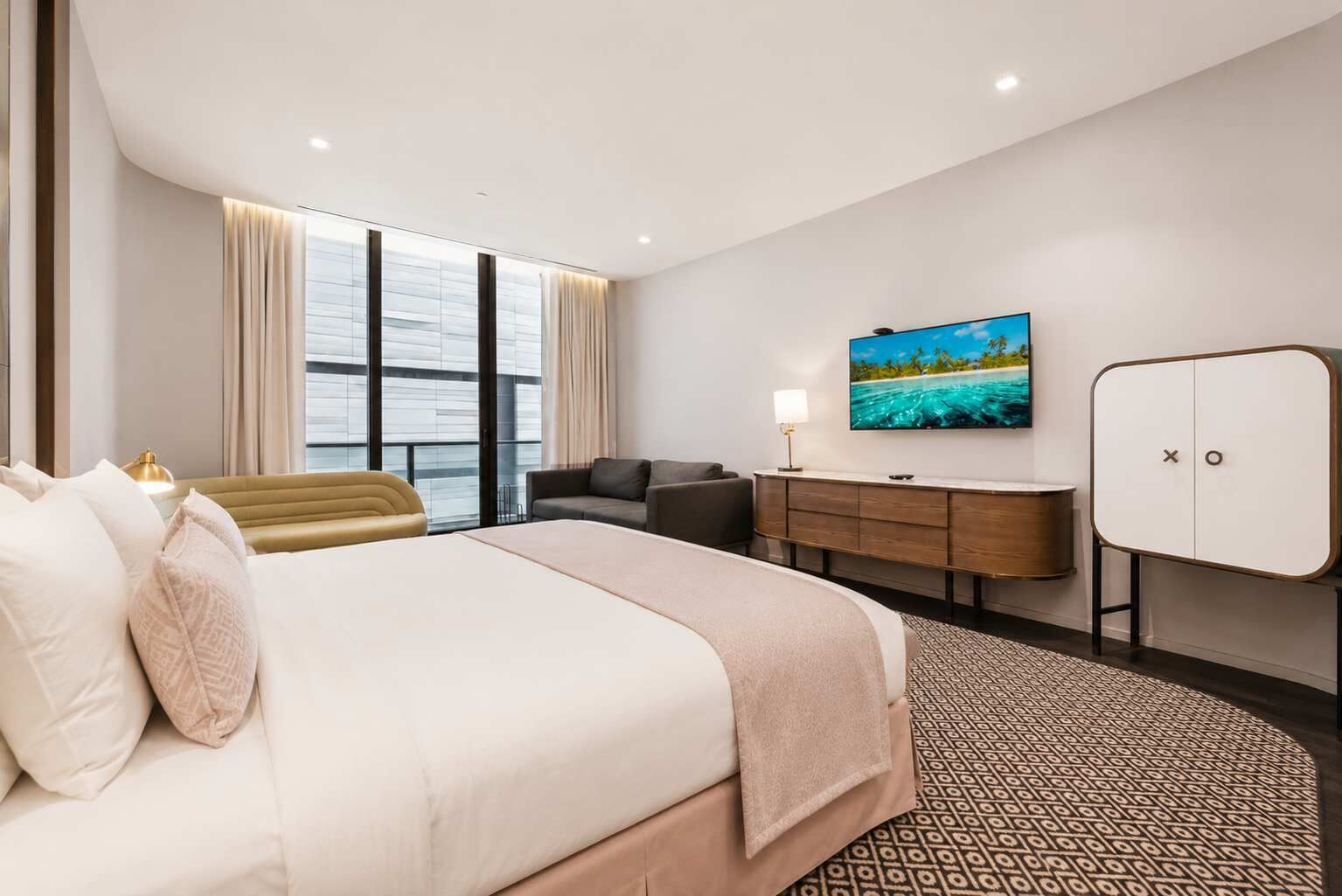 Une chambre d’hôtel avec un lit, un bureau, une télévision et une fenêtre avec des rideaux.