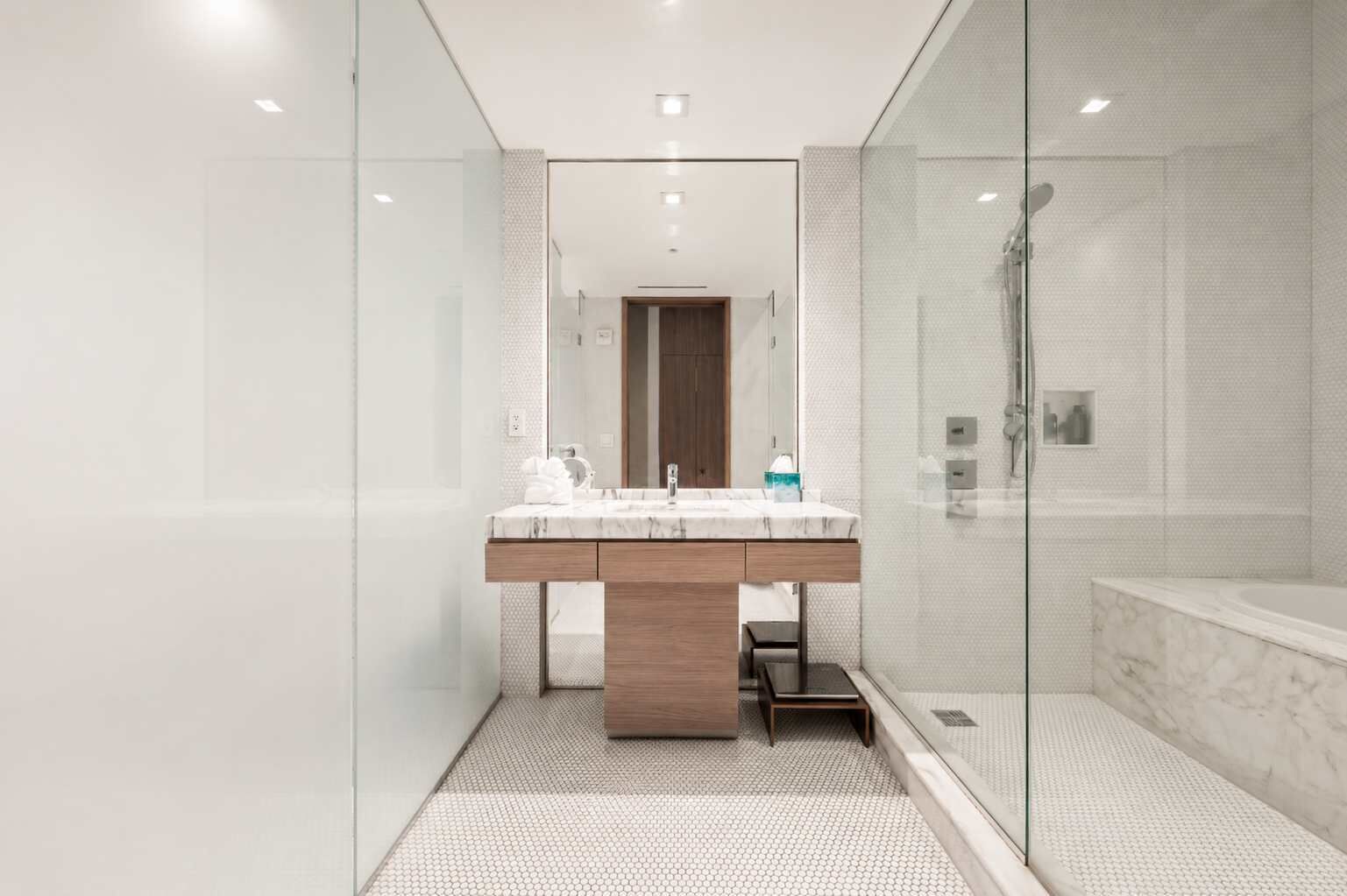 A modern bathroom with a glass-enclosed shower, a marble sink, and a wooden vanity.