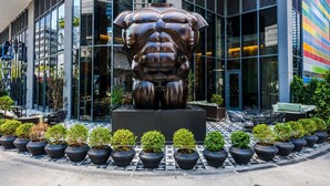Un edificio moderno con una grande scultura in bronzo antistante, circondato da piante in vaso e posti a sedere all'aperto.