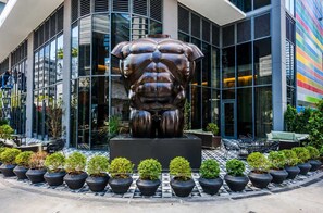 Ein modernes Gebäude mit einer großen Bronzeskulptur davor, umgeben von Kübelpflanzen und Außenmöbeln.