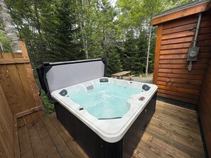 Un bain à remous doté d’une terrasse en bois, entouré d’une clôture en bois et d’arbres.