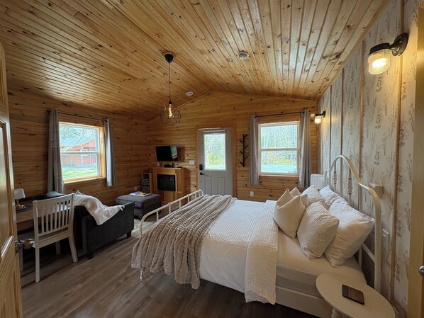 L’intérieur d’une cabane en bois, avec un lit, un bureau, un téléviseur et deux fenêtres.