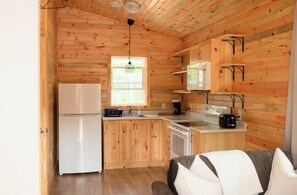 A compact kitchen with wooden walls, a refrigerator, a stove, and a sink.
