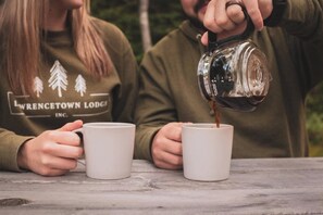 Two people at a table with white mugs, one pouring coffee into one of the mugs.