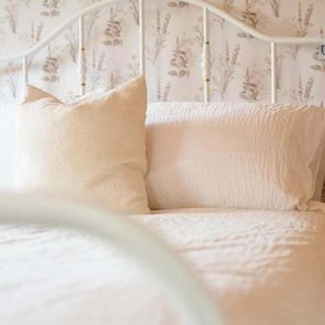 A bed with white bedding and a floral wallpaper pattern.