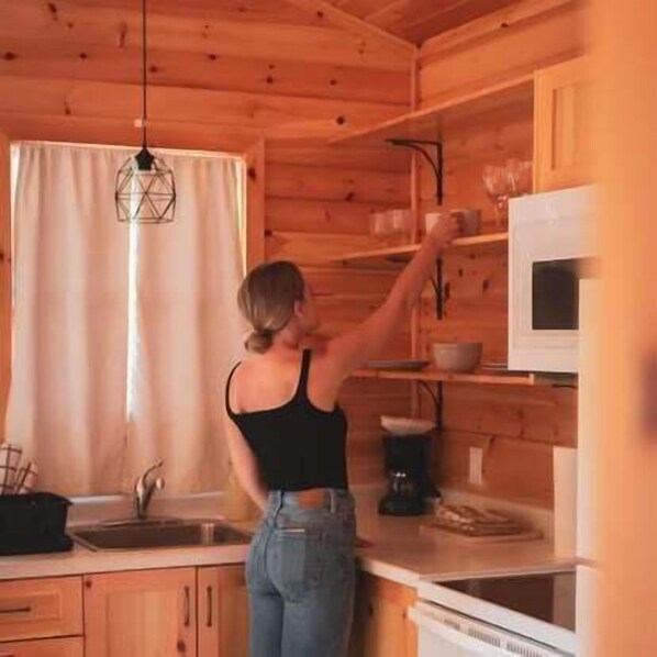 A kitchen with wooden cabinets, a sink, a microwave, and a hanging light fixture.