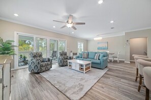A spacious living room with a ceiling fan, a blue sofa, patterned armchairs, a white coffee table, and a large window. - Salt & Pine at Lost Key Golf & Beach Club | Dog-Friendly | My Beach Getaways (Pensacola)
