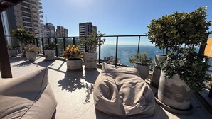 Una terrazza sul tetto con piante in vaso, un pouf beige e vista sullo skyline della città.