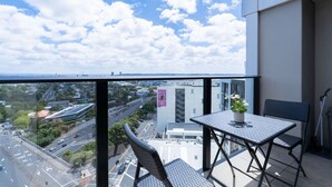 A balcony with a view of a cityscape, a table, two chairs, and a potted plant. - Urban Sunlit Nest in the Heart of CBD (Auckland Central)