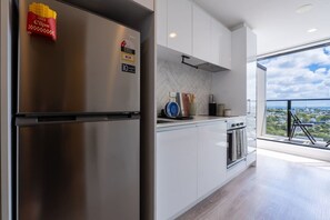 A modern kitchen with a stainless steel refrigerator, white cabinets, and a view of the city through large windows. - Urban Sunlit Nest in the Heart of CBD (Auckland Central)