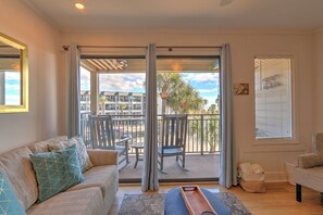 A living room with a sofa, chairs, a balcony with a table and chairs, and a window with blinds. - Ocean View Retreat - Just Steps from the Beach (Hilton Head Island)