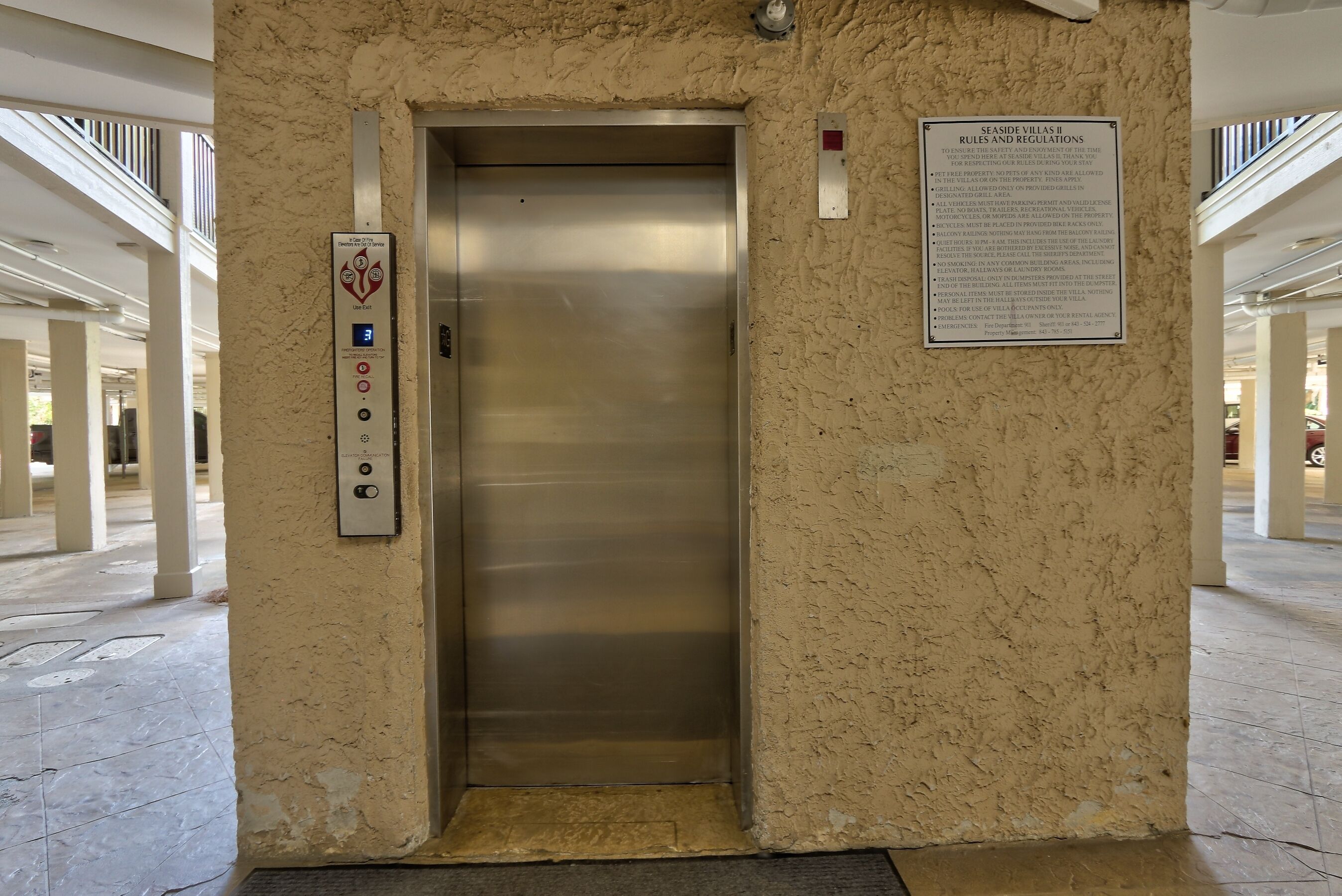 An elevator with a control panel, a sign with rules and regulations, and a textured wall.
