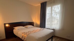 Una cama individual con cabecera de madera, una mesita de noche y una ventana con cortinas.