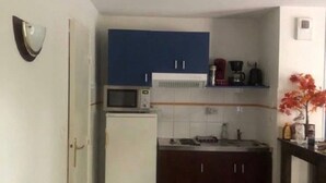Una cocina compacta con alacenas blancas, microondas, refrigerador y cafetera sobre la encimera.