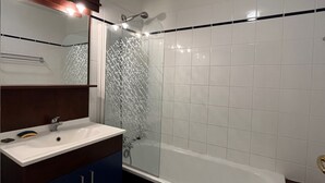 Un baño con lavamanos blanco, un espejo, ducha con puerta de cristal y una bañera.