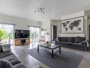 A modern living room with a large flat-screen TV, grey sofas, a coffee table, and a world map on the wall.