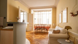Een woonkamer met een eethoek, een witte bank, een bijzettafeltje en een open haard.