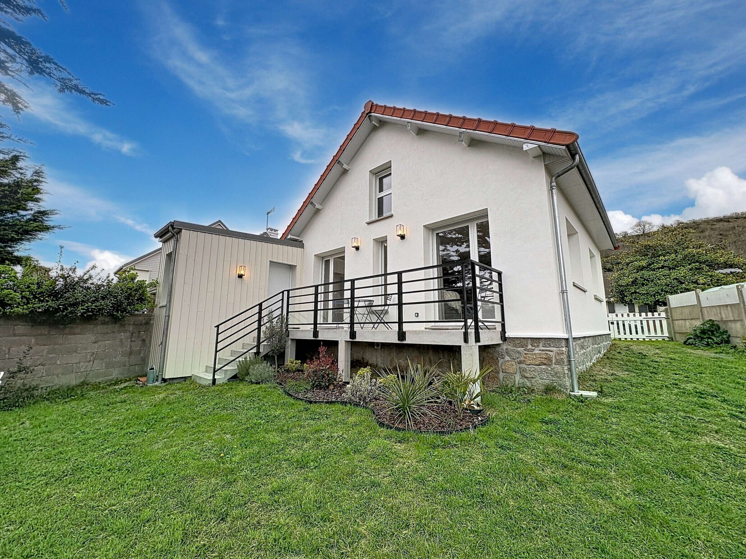 A two-story house with a balcony, a stone wall, and a grassy yard.