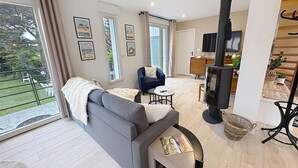 Una sala de estar moderna con un sofá, una mesita, una chimenea y un balcón con mobiliario de exterior.