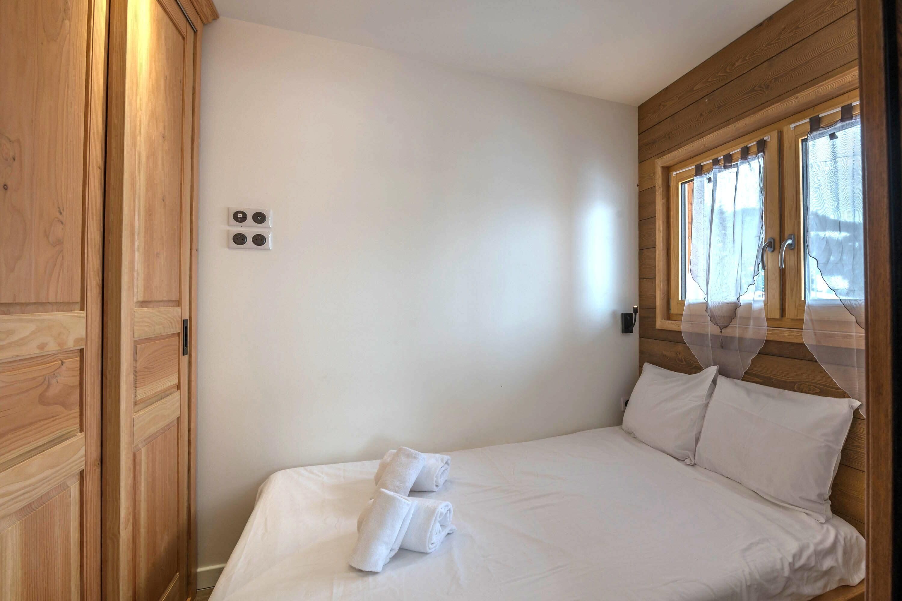 A bedroom with a wooden headboard, a bed with white linens, and a window with curtains.