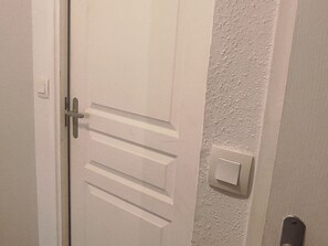 A white door with a handle and a light switch on the wall beside it. - Apartment for 6 in Super Besse with parking and pool (Besse-et-Saint-Anastaise-Super Besse)