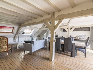 Une pièce de style « loft » avec des poutres apparentes, un coin repas comprenant une table et des chaises, un canapé et un petit espace cuisine.
